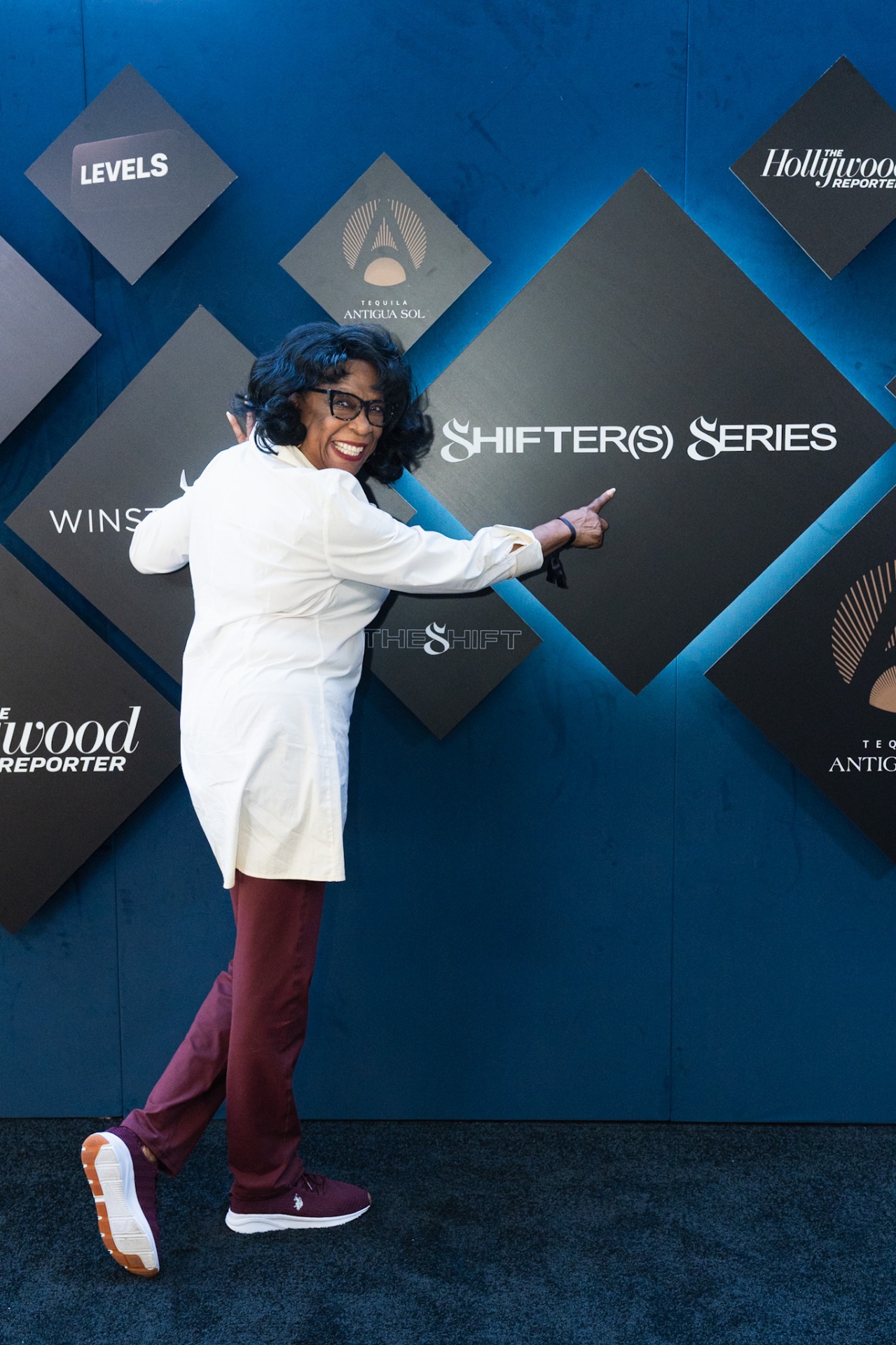 A guest pointing at the Shifter(s) Series step and repeat wall